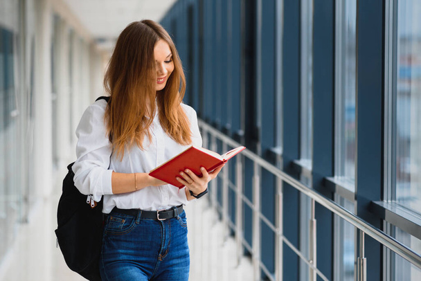 Positivity beautiful girl smiling at camera, standing on corridor with notes as backpack, going to lesson. Happy brunette female student studying in luxury university. - Φωτογραφία, εικόνα