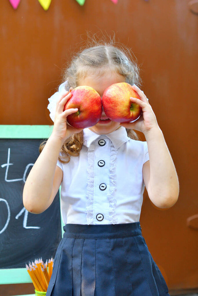 Muotokuva kaunis nuori ensiluokkalainen jäähyväiskello. tiedon päivä. lukuvuoden alussa. Tyttö, jolla on omena kasvoillaan. tiedon päivä
 - Valokuva, kuva