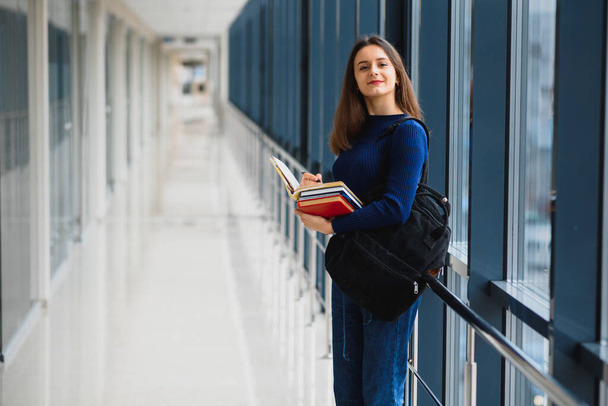 Positivity beautiful girl smiling at camera, standing on corridor with notes as backpack, going to lesson. Happy brunette female student studying in luxury university. - Foto, Imagem