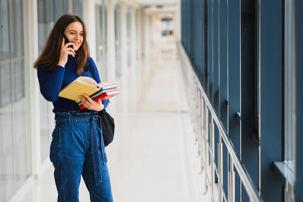 Portrait of a pretty female student with books and a backpack in the university hallway - Photo, image