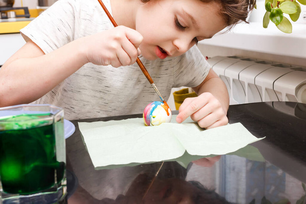 Junge taucht ein Ei in ein Glas mit Farbe. Junge bemalt Ostereier - Foto, Bild