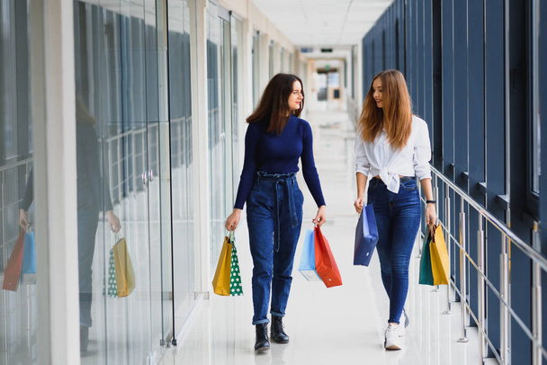 Two girl-friends on shopping walk on shopping centre with bags - Foto, Imagen