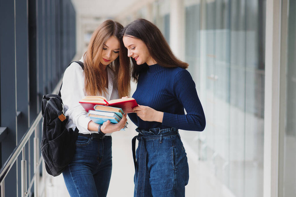 Two young female students standing with books and bags in the hallway University speaking each other. - Zdjęcie, obraz