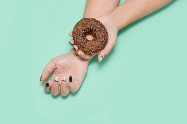 A woman's hand with a beautiful manicure holds a chocolate doughnut with powder on a light background. - Foto, Bild