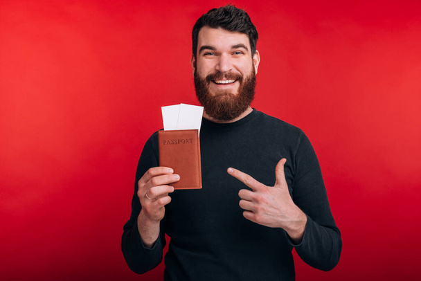 joven guapo feliz señalando el pasaporte y los billetes
 - Foto, Imagen