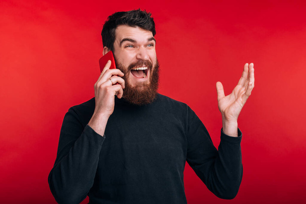 angry man screaming and talking on smartphone while standing over red background - Zdjęcie, obraz