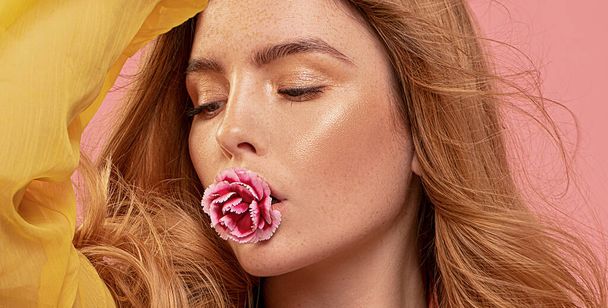 Stunning girl holds flower in mouth. Beautiful woman with red long hair. Woman with natural freckles. Skin care concept. Spring,summer. - Foto, imagen