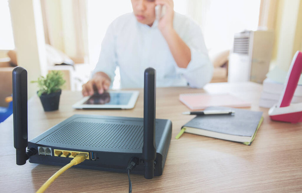 closeup of a wireless router and a man using smartphone on living room at home ofiice, equipment for  working from home, while in quarantine isolation during the Covid-19 health crisis.        - Photo, Image
