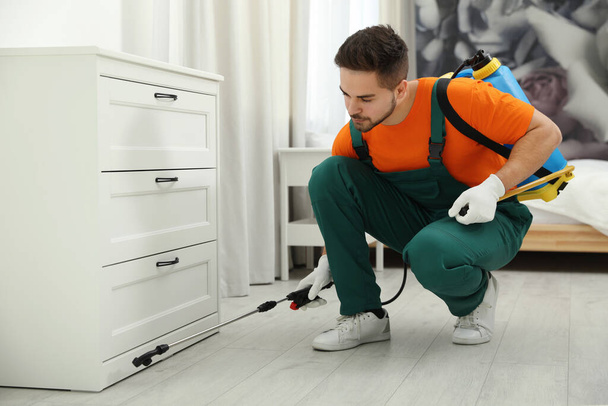 Pest control worker spraying insecticide near chest of drawers indoors - Foto, Imagen