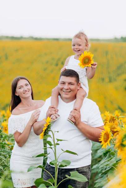 happy family having fun in the field of sunflowers. Father holding his daughter. Mother holding sunflower. outdoor shot - Fotó, kép