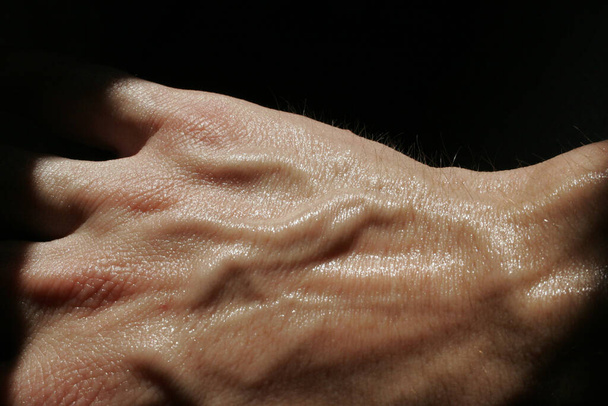 ραχιαία ενός ιδρωμένου χεριού με πολλές φλέβες σε μαύρο φόντο - Φωτογραφία, εικόνα