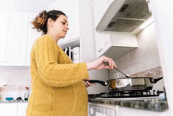 Kontrapunkt-Foto einer schwangeren Frau mit gelbem Pullover, die mit ernstem Gesichtsausdruck in einer Küche steht - Foto, Bild