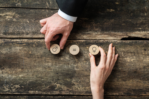 Igualdad de género imagen conceptual - mano masculina y femenina colocando círculos cortados de madera con símbolos de género sobre un escritorio de madera rústico
. - Foto, imagen