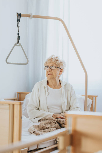 Grandmother with glasses is sitting on the bed in the nursing home - Foto, Bild