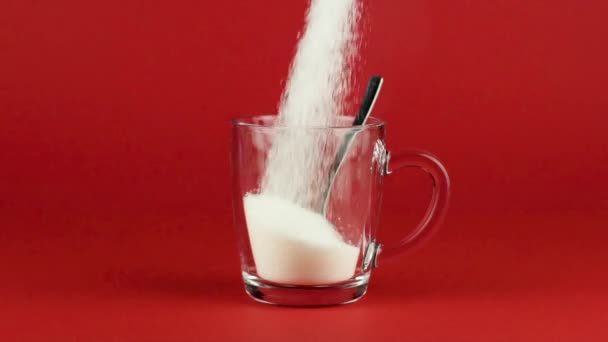 Wlać szklankę kubek cukru z łyżeczką do herbaty czerwony kontrastujące tło zwolniony ruch - Materiał filmowy, wideo
