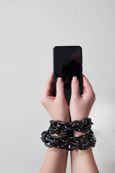 Catena di ferro che lega mano e smartphone nel concetto di social media e dipendenza da internet su sfondo grigio - Foto, immagini