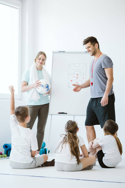 Young handsome teacher and his female assistant explain the tactics to children before the important match - Fotografie, Obrázek