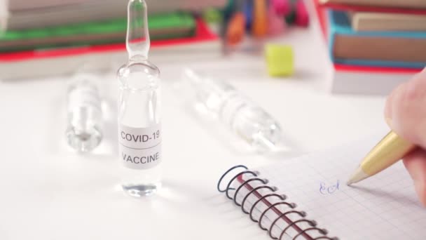 Lugar de trabajo médico con ampollas con vacuna de COVID-19 y libros. El médico escribe en un cuaderno los resultados de las pruebas de un medicamento para el coronavirus. Primer plano
 - Metraje, vídeo
