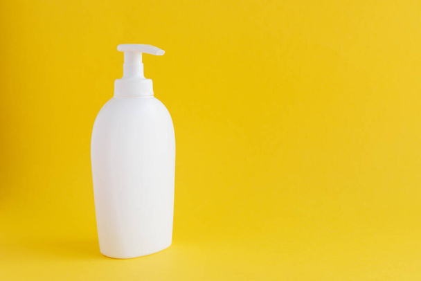 Biała plastikowa butelka z dozownikiem do mydła w płynie, kremu lub środka dezynfekującego znajduje się na żółtym tle. Przestrzeń kopiowania. - Zdjęcie, obraz