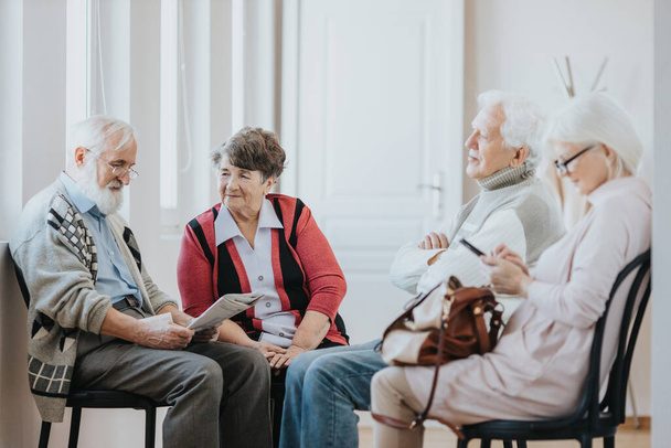 Group of older people sitting on a corridor waiting in a line to doctor's office - Foto, imagen