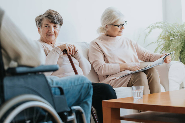 Duas mulheres idosas com deficiência sentadas em uma sala comum e esperando o médico
 - Foto, Imagem