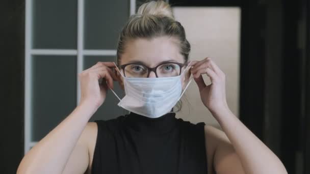 Girl, woman puts on a medical protective mask looks at the camera. Coronavirus quarantine concept. The woman is locked. Quarantine. face mask - Filmmaterial, Video