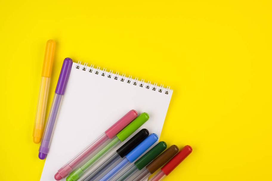 markers of different colors with a white Notepad on a yellow background, top view. colorful pens with a notebook close up - Φωτογραφία, εικόνα
