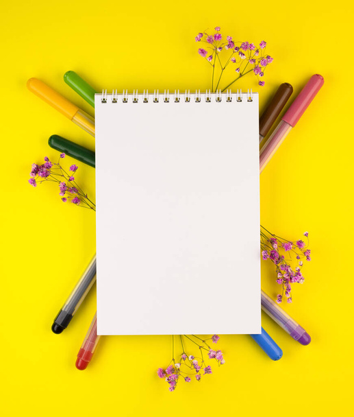 markers of different colors with a white Notepad on a yellow background, top view. colorful pens are spread out under the notebook close up - Φωτογραφία, εικόνα