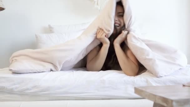 Joyful woman hiding under the blanket, looking at the camera and smiling. Slowmotion. - Video, Çekim