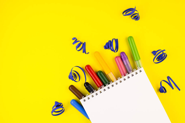 markers of different colors with a white Notepad on a yellow background, top view. colorful pens are spread out under the notebook close up - Foto, afbeelding