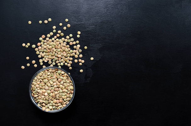 lentils in a glass bowl and scattered nearby on a black slate background with place for text. healthy eating pattern. veganism. lean foods. - Φωτογραφία, εικόνα