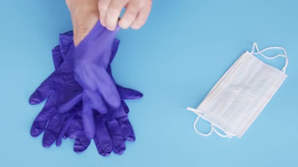 Doctor or nurse putting on medical latex gloves and taking protective respiratory mask, blue background view from above, 4k - Video