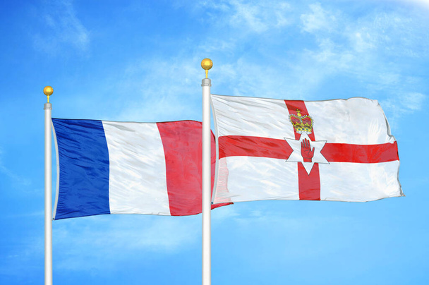Γαλλία και Βόρεια Ιρλανδία δύο σημαίες σε κοντάρια σημαίας και μπλε θολό φόντο του ουρανού - Φωτογραφία, εικόνα