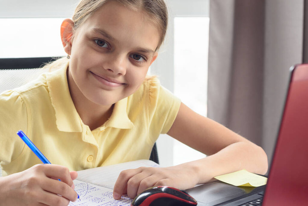 Lähikuva muotokuva onnellinen tyttö tekee kotitehtäviä edessä tietokoneen näytön
 - Valokuva, kuva