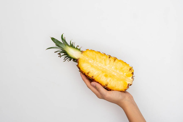 Female hand holding a half of ripe pineapple on a white background. - Foto, Imagen