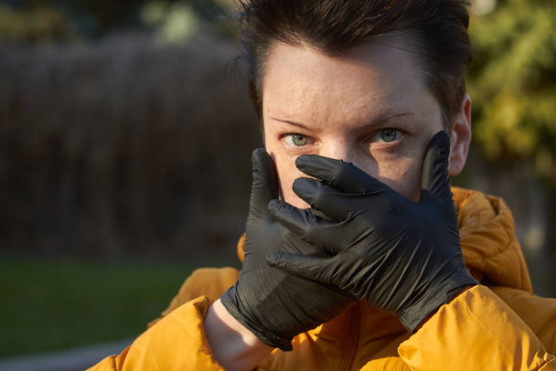 Una mujer europea de mediana edad con guantes negros protectores hace un gesto de advertencia durante la epidemia de coronavirus COVID-19
 - Foto, imagen
