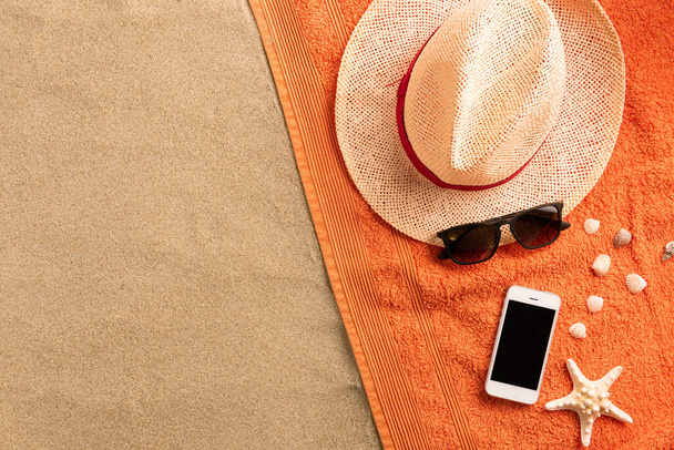 Summer fashion, summer outfit on sand background. Smartphone, sunglasses and straw hat. Flat lay, top view - Photo, image