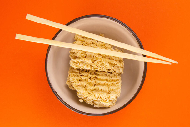 Instant noodles with wood sticks. Asian fast food on a orange background close-up. Top views. - Photo, Image
