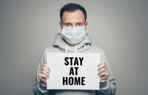Studio portrait of young men wearing a face mask and gloves holding board with stay at home text. Coronavirus pandemic, dust allergy, protection against virus - Fotó, kép