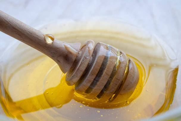 Honey dipper on the bee honeycomb background. Honey tidbit in glass jar and honeycombs wax. - Photo, Image