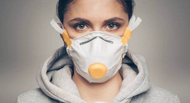 Studio portrait of young woman wearing a face mask, looking at camera, close up on gray background. Coronavirus pandemic, dust allergy, protection against virus concept - Fotoğraf, Görsel