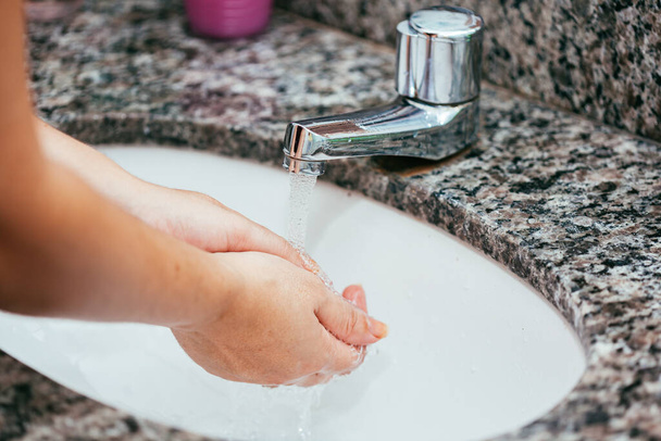 Een vrouw waste haar handen met water en zeep bij de wastafel. Coronavirus en Covid-19 preventie - Foto, afbeelding