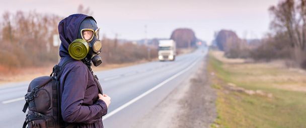 A girl in a black gas mask stands on the edge of a suburban highway.  - Photo, image