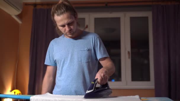 Young handsome man ironing clothes with an iron. Womens work that a man does. - Кадры, видео