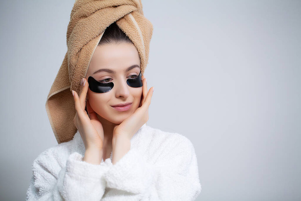 Hermosa mujer con un abrigo blanco aplica parches en los ojos para el cuidado de la piel
 - Foto, Imagen