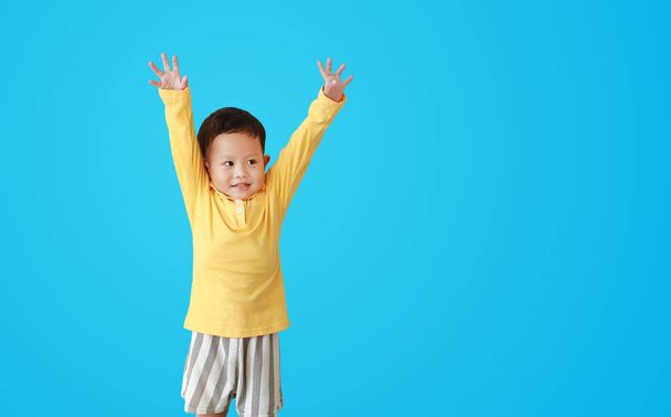 Portré mosolygós kis ázsiai kisfiú kifejezés emelje fel a kezét, és keres mellett elszigetelt kék háttér fénymásolás hely. - Fotó, kép