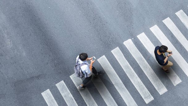 Menschliches Leben in sozialer Distanz. Luftaufnahme mit verschwommenem Mann mit Smartphone am Fußgängerüberweg auf grauem Gehweg mit Leerraum. - Foto, Bild
