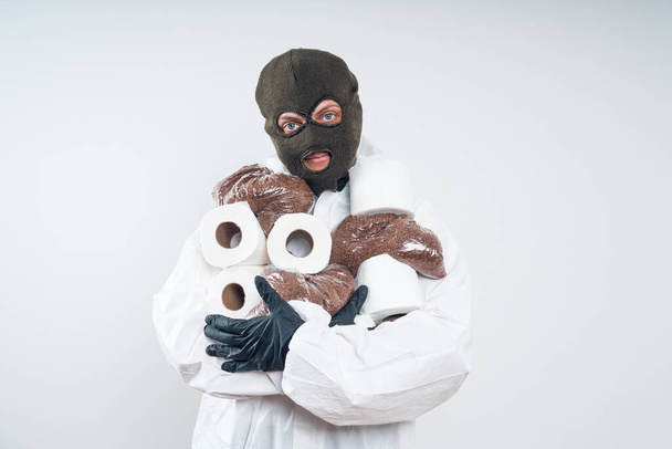 Robber in a mask and white suit holds a buckwheat and toilet paper. - Fotó, kép