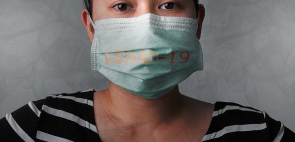 Μια χοντρή Ασιάτισσα που φοράει μάσκα προσώπου για προστασία από την ατμοσφαιρική ρύπανση ή την επιδημία του ιού σε γκρι φόντο. Έννοια υγειονομικής περίθαλψης. - Φωτογραφία, εικόνα