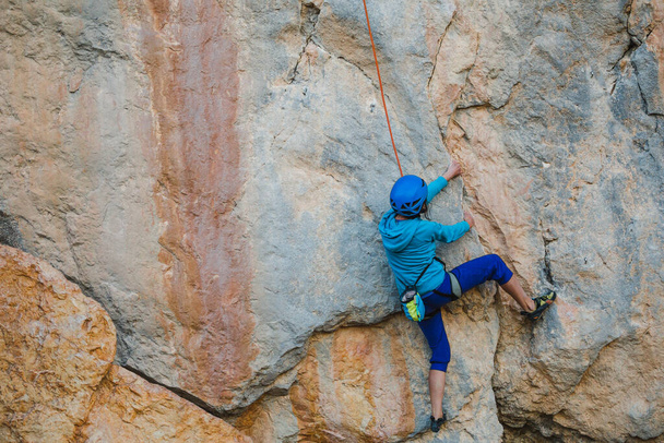 Eine Frau mit Helm erklimmt einen wunderschönen orangefarbenen Felsen. Kletterschutzausrüstung. Sicherheit beim Klettern. Bergsteiger überwindet eine schwierige Route in natürlichem Gelände. Klettern in der Türkei. - Foto, Bild